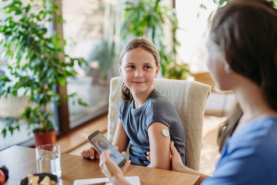 Girl with diabetes checking blood glucose level at home using continuous glucose monitor. Girl's mother connects CGM to a smartphone to monitor blood sugar levels in real time.