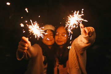 Cheerful young Asian female friends are holding sparklers and having fun 