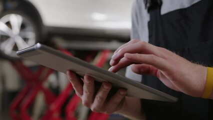 Hands of an auto electrician with a tablet. Diagnostics and repair of cars at a service station