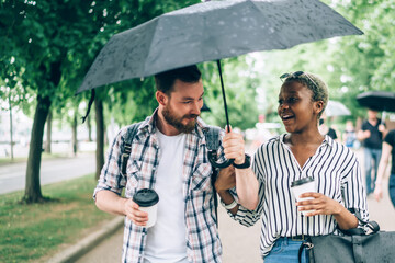 Cheerful multiracial couple walking under rain
