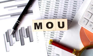 MOU text on wooden block on graph background with pen and magnifier