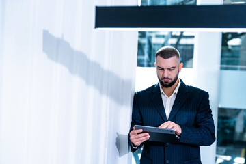 Handsome businessman with digital tablet computer looking in device screen working in modern business center of big corporation.