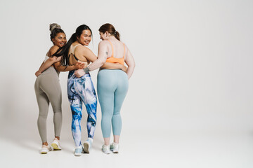 Obraz premium Back view of smiling women in sportswear posing together isolated over white background