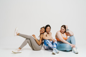 Group of joyful women in sportswear posing together while sitting isolated over white wall