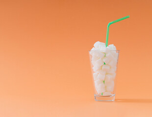 Creative composition made of glass full of sugar cubes with green drinking straw on pastel orange background. Minimal unhealthy diet concept. Be healthy lifestyle idea. Copy space.