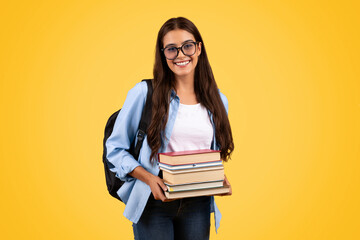 Happy teen student lady with backpack in glasses hold many books, enjoy study
