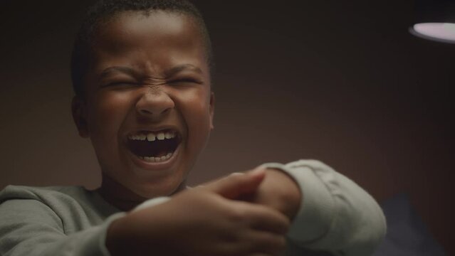 Medium closeup of frightened African American little boy screaming out loud from nightmare in dark room light flickering