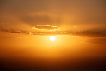 Sunset through and behind the cloud over the sea background. Sunbeam colors golden the sky