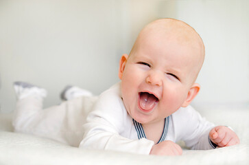 Three month old very happy baby boy lying on the belly in white room wearing white one-piece