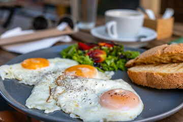 Fried egg with pepper, salad, toasted bread in dish and a blur cup of coffee on wooden table.