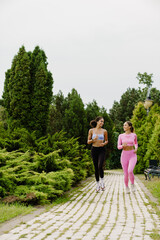 Fototapeta na wymiar Portrait of two smiling women running together in park