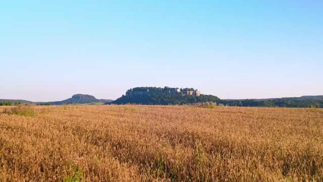 4K aerial drone flight over a field with fortress K&ouml;nigstein in the background. The river Elbe flows through the valley at the foot of the fortress.