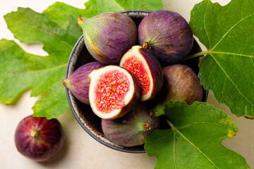 Bowl with fresh ripe purple figs fruit with green leaves. Top view.