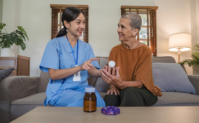 Asian caregiver nurse give consult to Caucasian senior woman 60s patient. Attractive care pharmacist hold medicine pills bottle, explain prescription to elderly mature grandmother in living room.