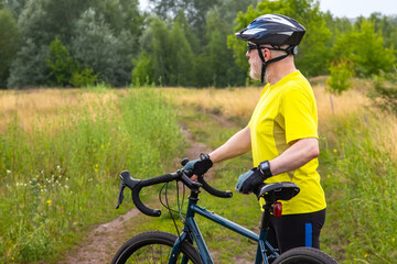 Fototapeta premium bearded man cyclist in yellow clothes is resting on a bicycle on the road in nature. sports, hobbies and entertainment for health