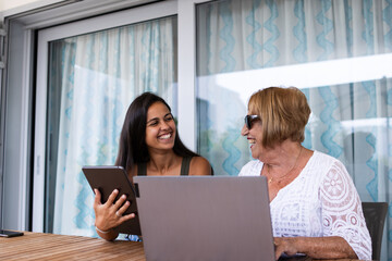Two generations of women are sitting at the terrace table using digital technology together.
