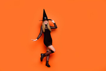 Full body photo of charming mysterious conjurer girl arm touch headwear empty space isolated on orange color background
