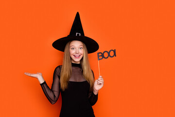 Photo of attractive blonde teen woman hold palm empty space boo sign dressed black halloween clothes isolated on orange color background