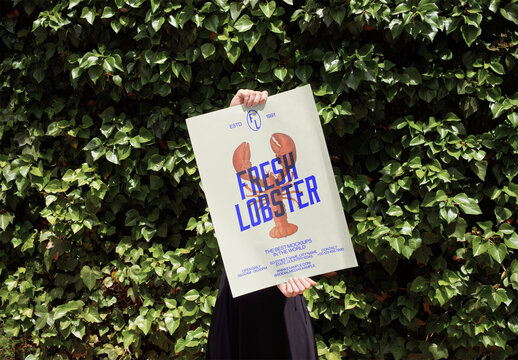 Mockup of person holding customizable vertical A2 poster by hedge