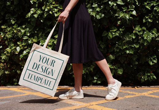 Mockup of young woman holding customizable tote bag by hedge