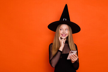 Photo of tricky cunning lady wear black wizard costume cap typing halloween greetings looking empty space isolated orange color background