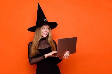 Photo of cute excited girl dressed dark witch dress headwear texting emails modern device empty space isolated orange color background