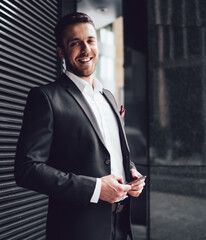 Fototapeta premium Pleasant man in classical suit with smartphone looking at camera with smile in street in downtown