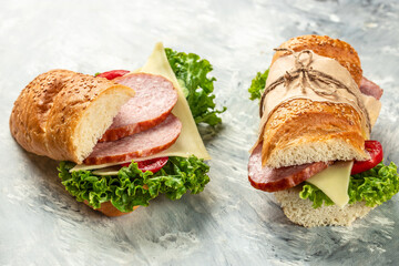 two fresh baguette sandwiches with salami, tomato, lettuce and cheese on a light background top view. place for text