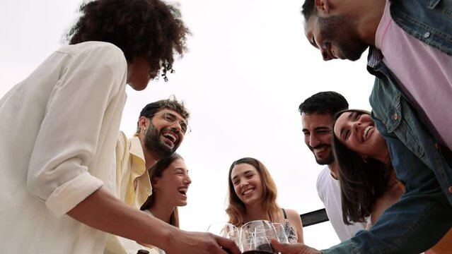 Cheerful carefree group of friends standing and toasting with wine glasses in a terrace.Diverse group of young people celebrating and drinking wine in a rooftop dinner.