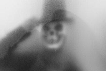 Bangkok, Thailand - August, 20, 2023 : Shadow blur of horror man in ghost skull mask.Dangerous man behind the frosted glass.Mystery man.Blur picture.Add effects noise and grain.Concept Halloween.