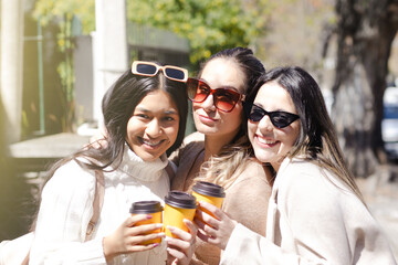 Three young women look at the camera clinking their recyclable coffee cups.