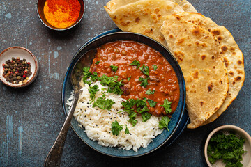 Traditional Indian Punjabi dish Dal makhani with lentils and beans in black bowl served with basmati rice, naan flat bread, fresh cilantro and spoon on blue concrete rustic table top view. - obrazy, fototapety, plakaty