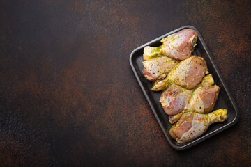 Raw uncooked chicken legs in green marinade with seasonings in black plastic container top view on dark rustic background. Preparing healthy meal with marinated chicken drumsticks, copy space. - obrazy, fototapety, plakaty