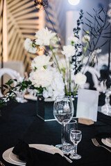 Wedding set up, dinner table reception. Serving, setting newlyweds table. Plate and glass, stack, wineglass, luxury rich decor, black napkin. Birthday, event. Restaurant interior. Side view.