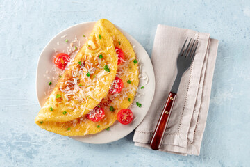 An omelet with tomato and parsley, eggs for breakfast, a healthy vegetarian dish with cheese, overhead flat lay shot with a fork - obrazy, fototapety, plakaty