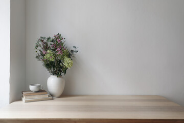 Fototapeta na wymiar Elegant Scandinavian interior. Vase with floral bouquet. Eucalyptus tree branches, hydrangea, wax flowers. Cup of tea, cofffe. Old books. Empty wall background. Modern living room, home office.