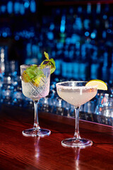 elegant glasses of tasty cocktails with garnishments with bar on backdrop, concept