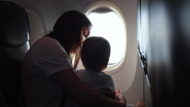 Joyful mother shows view from plane window to toddler girl. Child cradled in arms of mother as family embarks on memorable vacation together