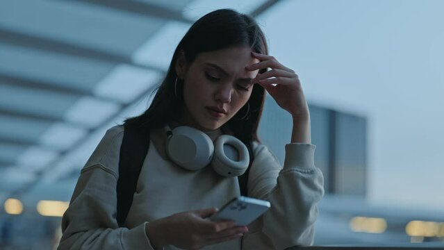 A modern young woman, backpack on, uses her smartphone while traveling, appearing sad and stressed in the evening