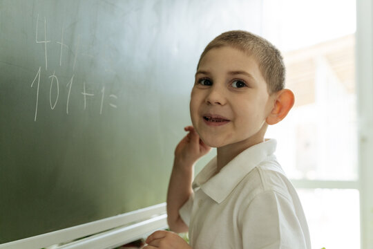 Happy smiling little kid boy writes mathematics on the board