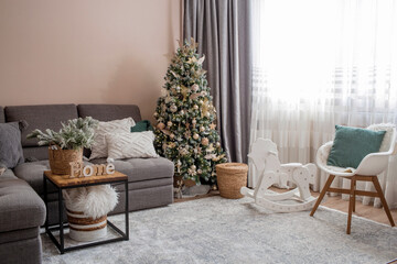 New Year holidays 2023. Cozy decor in gray-green tones in the interior of the Christmas room, a Christmas tree decorated with garlands, gifts, a wooden horse. A festive living room in the house.