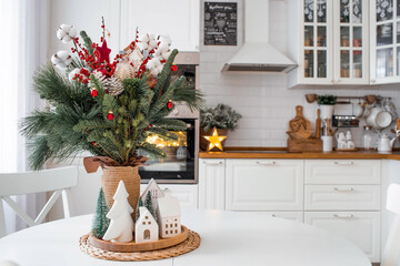 A spruce bouquet with red berries, toys, cotton on a white kitchen table. Christmas decorations in the interior. The concept of preparation for the New Year's holiday 2024.