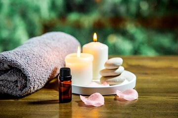 Fototapeta na wymiar spa still life with candles, towel and essetial oil against green nature background on wooden table