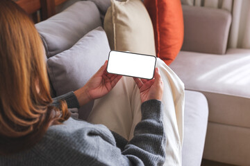 Mockup image of a woman holding mobile phone with blank desktop white screen while lying on a sofa at home - obrazy, fototapety, plakaty