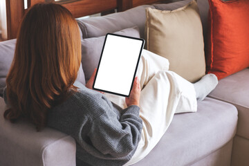 Mockup image of a woman holding digital tablet with blank desktop screen while lying on a sofa at home