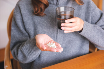 Closeup image of a woman holding pills and a glass of water