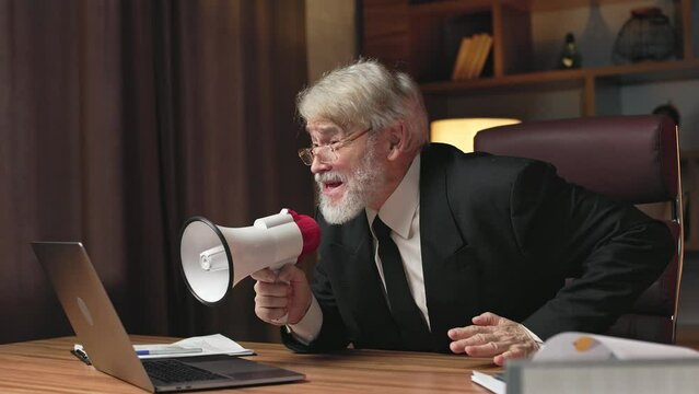 Side view of aggressive senior man in formal wear shouting at web conference attendee via loudspeaker at work. Furious general manager loosing temper because of missed deadline of important project.