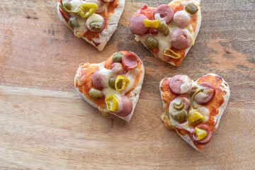 Heart shaped mini pizzas for Valentine's Day on wooden background.
