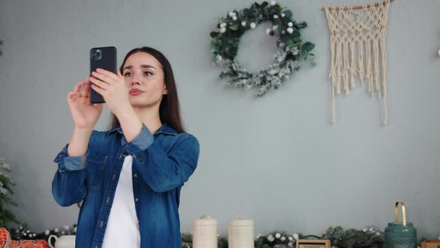 Concerned upset young woman in a Christmas-decorated kitchen puzzled over malfunctioning phone, facing loss of WiFi, 3G cellular coverage and data during the festive New Year and Christmas season.