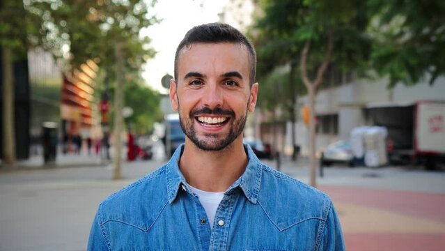 Close up portrait of handsome guy with perfect white teeth smiling and looking at camera standing outdoors. Front view of young man with friendly and positive expression. Happy adult male staring